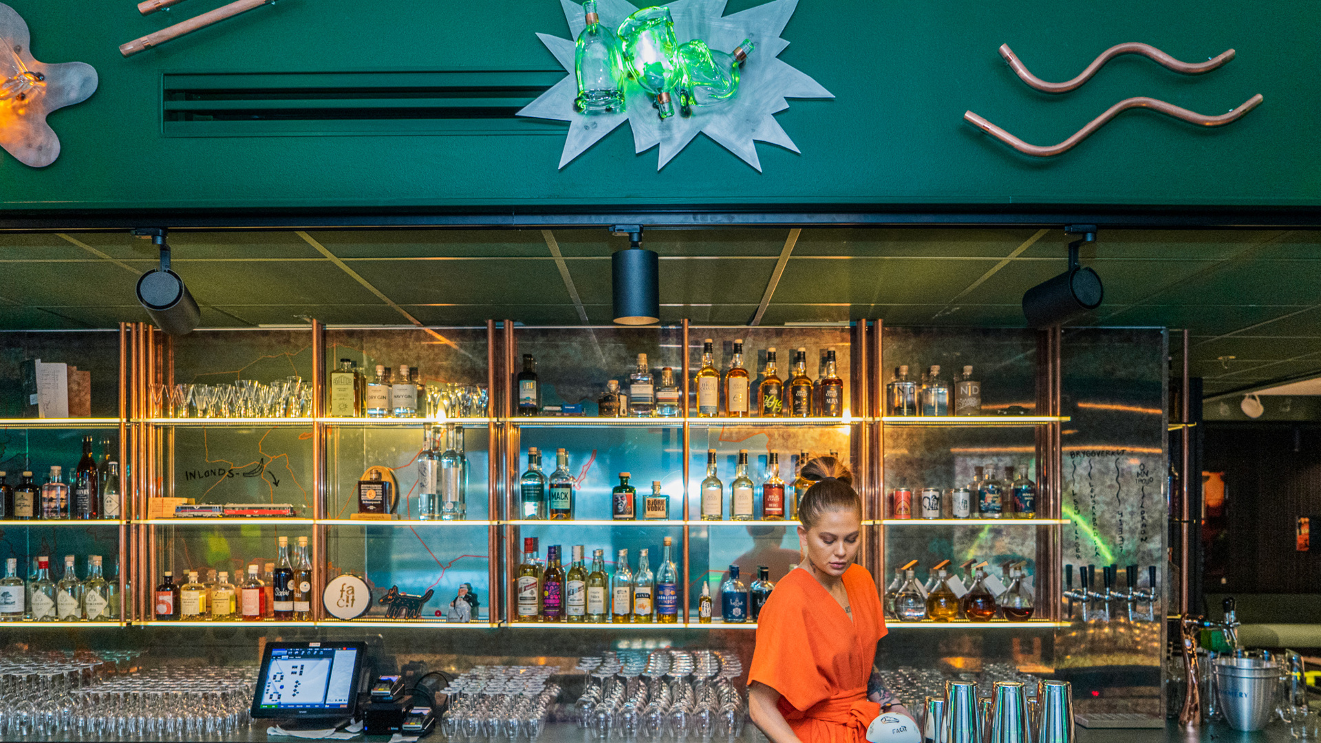 Facit Bar. A woman in an orange dress is standing in a green bar.