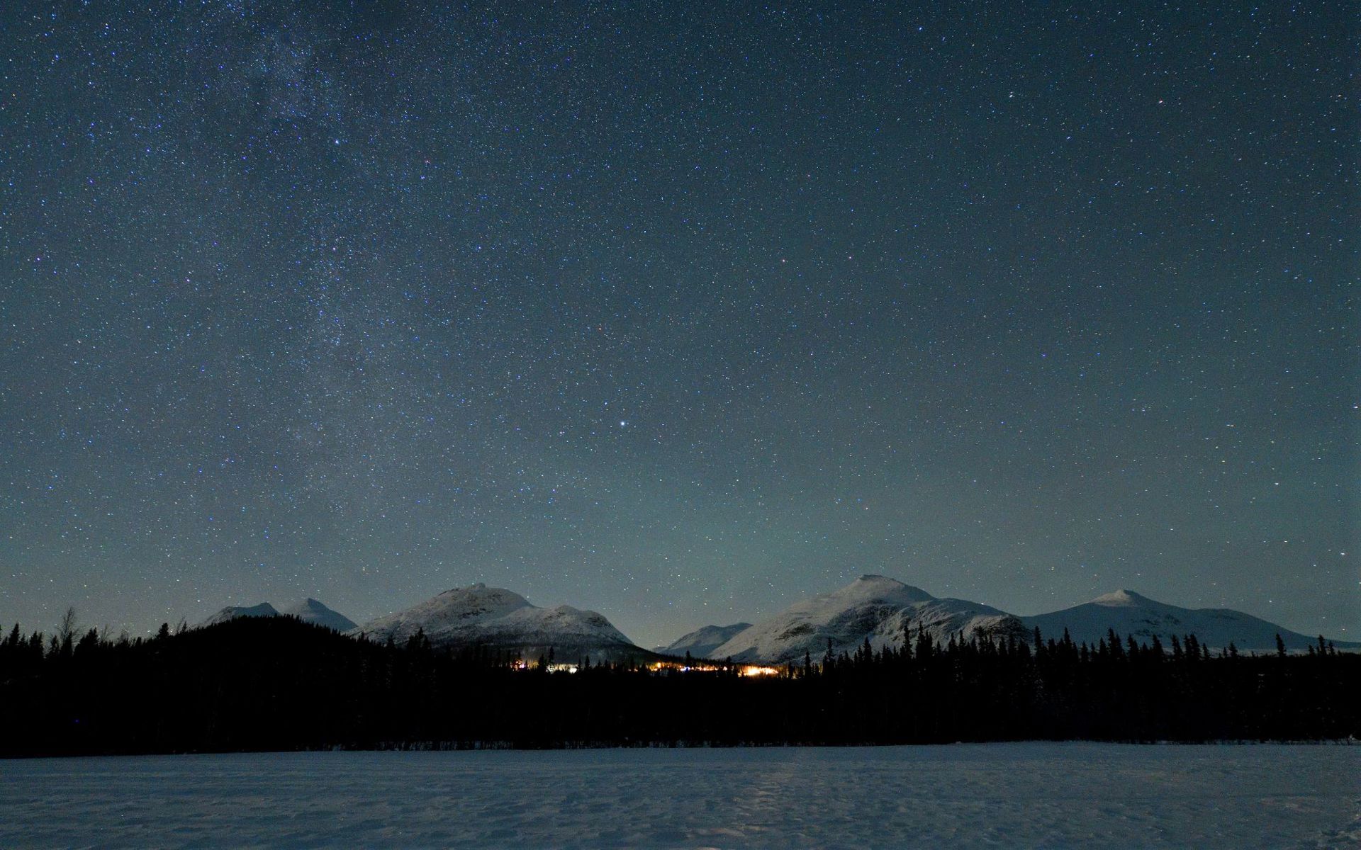 A sky full of stars over white mountains and a small village. 