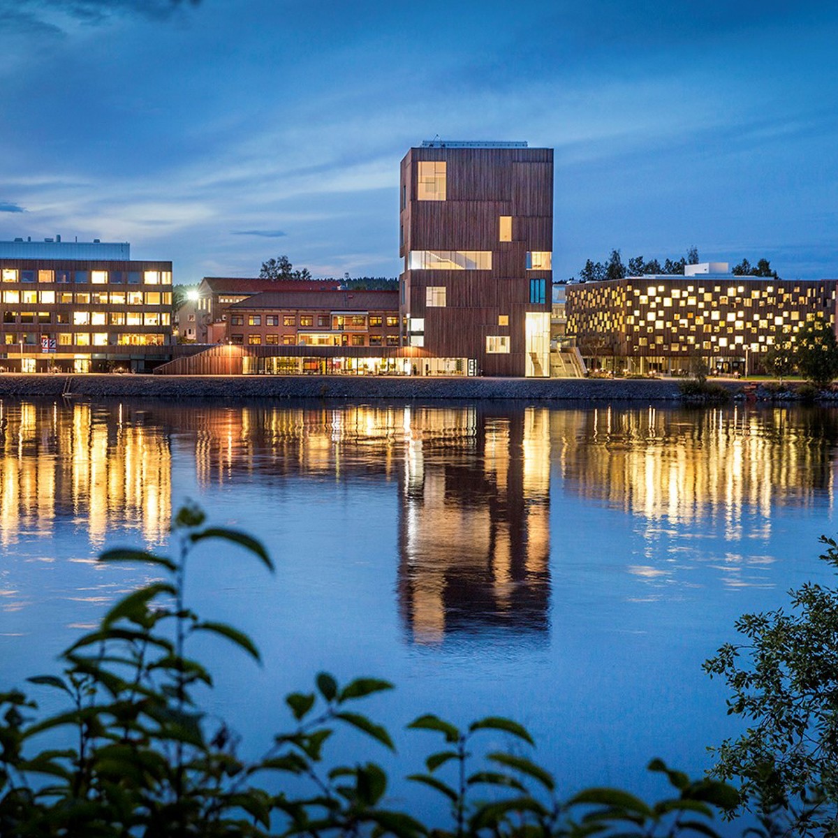 An evening photo of arty buildings. Lights from the windows are reflected on the water in the foreground. 