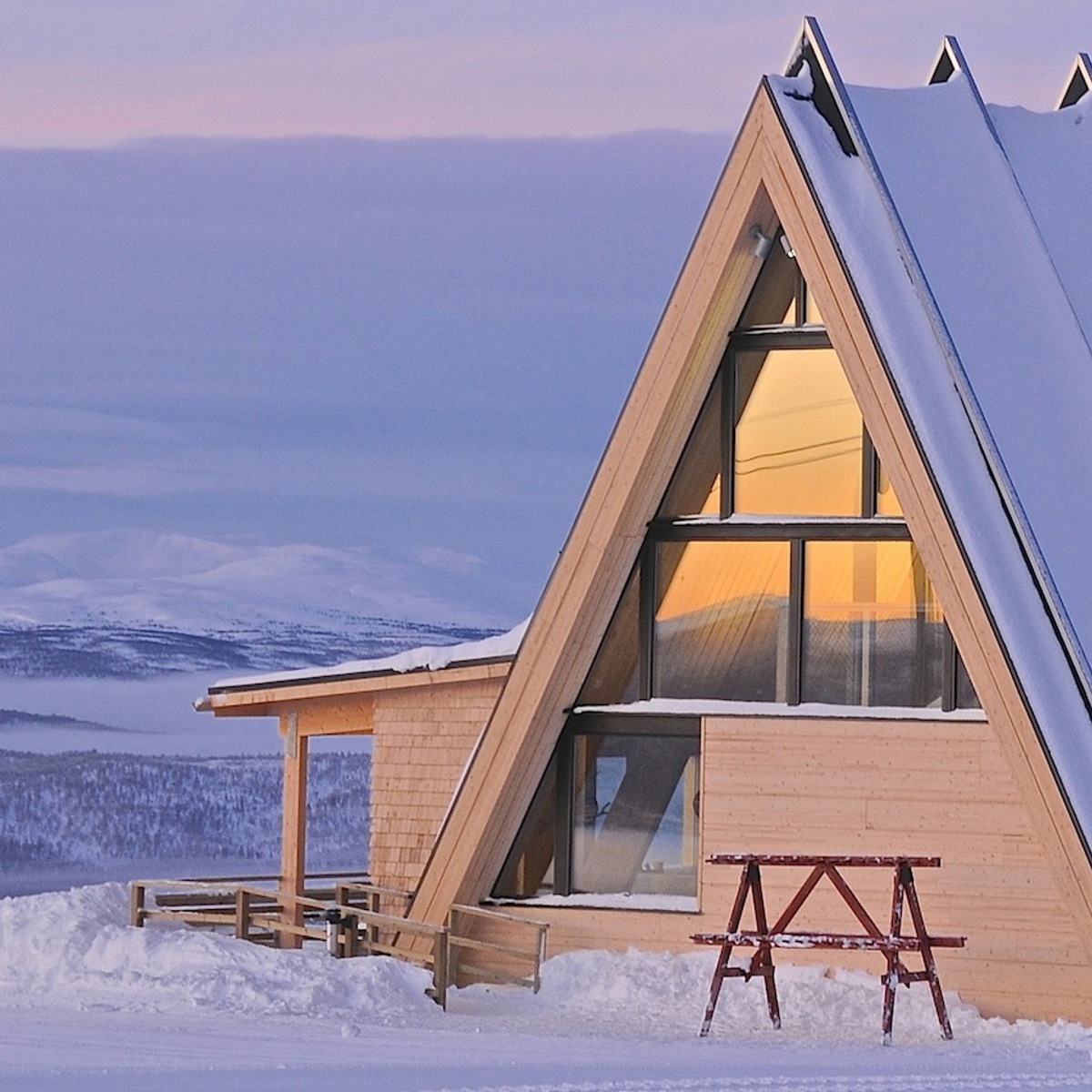 A building covered in snow, with snowy mountains in the background. 