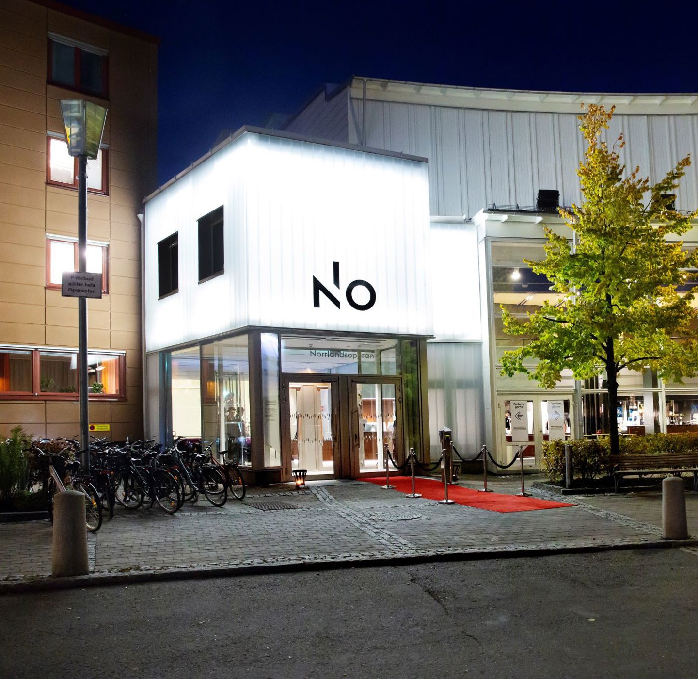 A picture of a building with a strong white neon sign that light up the street in front of it. 