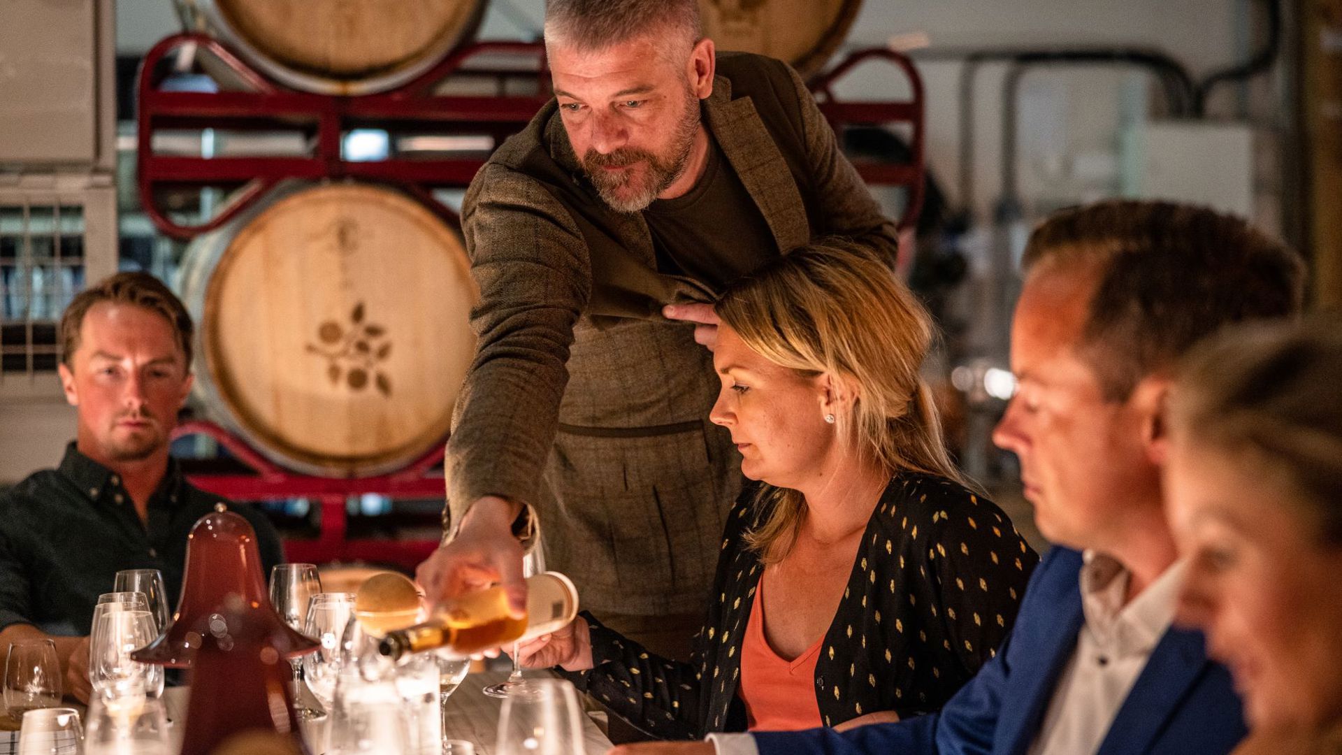 Brännland Iscider Foto: Visit Umeå A man pouring cider in a womans glas, suppounded by casks.