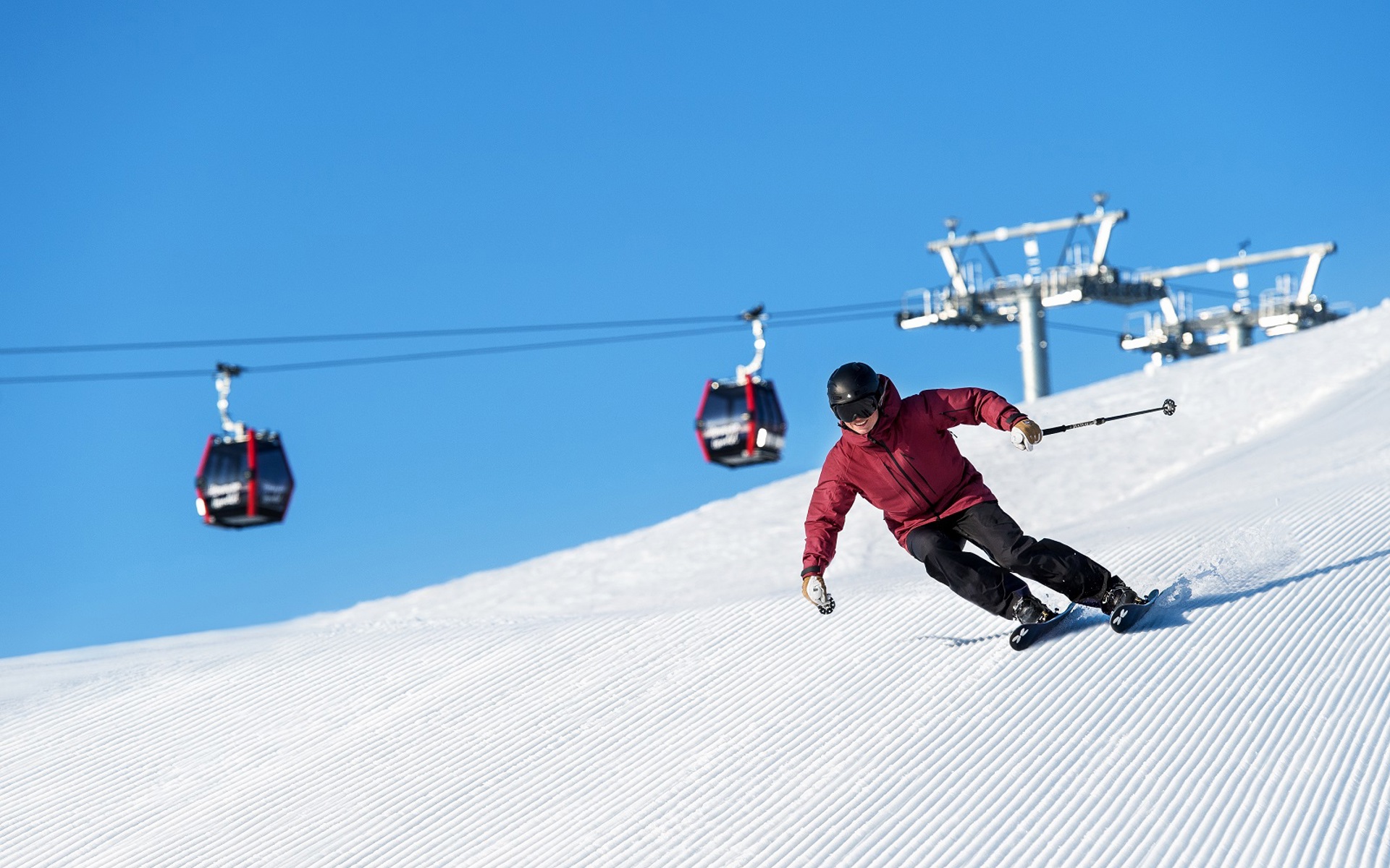 A skier doing turns on a slope with blue sky and a gondola in the background. 