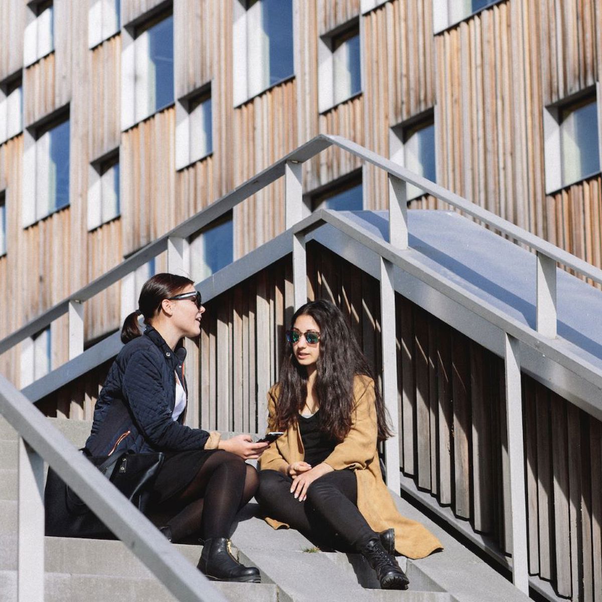 Two women sitting on a stair soaking up the sun. 